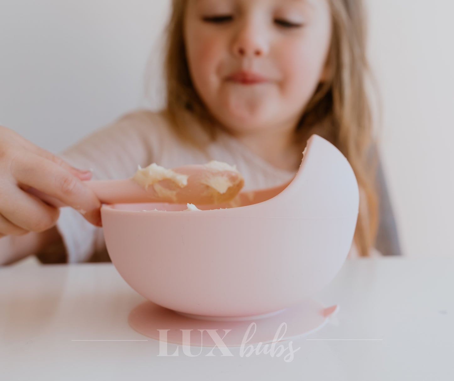 Child holding a pink bowl with food, blurred background