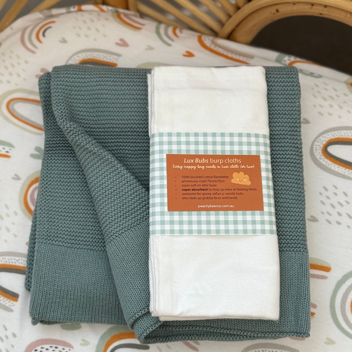 Folded green and white blanket with a label on a crib with patterned sheets.