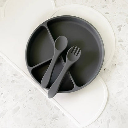 Gray children's plate with divided sections, spoon, and fork on a white textured surface