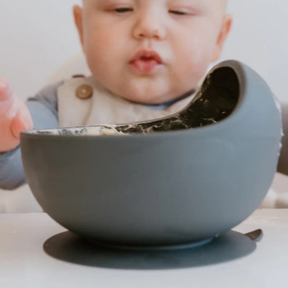 Baby interacting with a gray bowl on a white surface