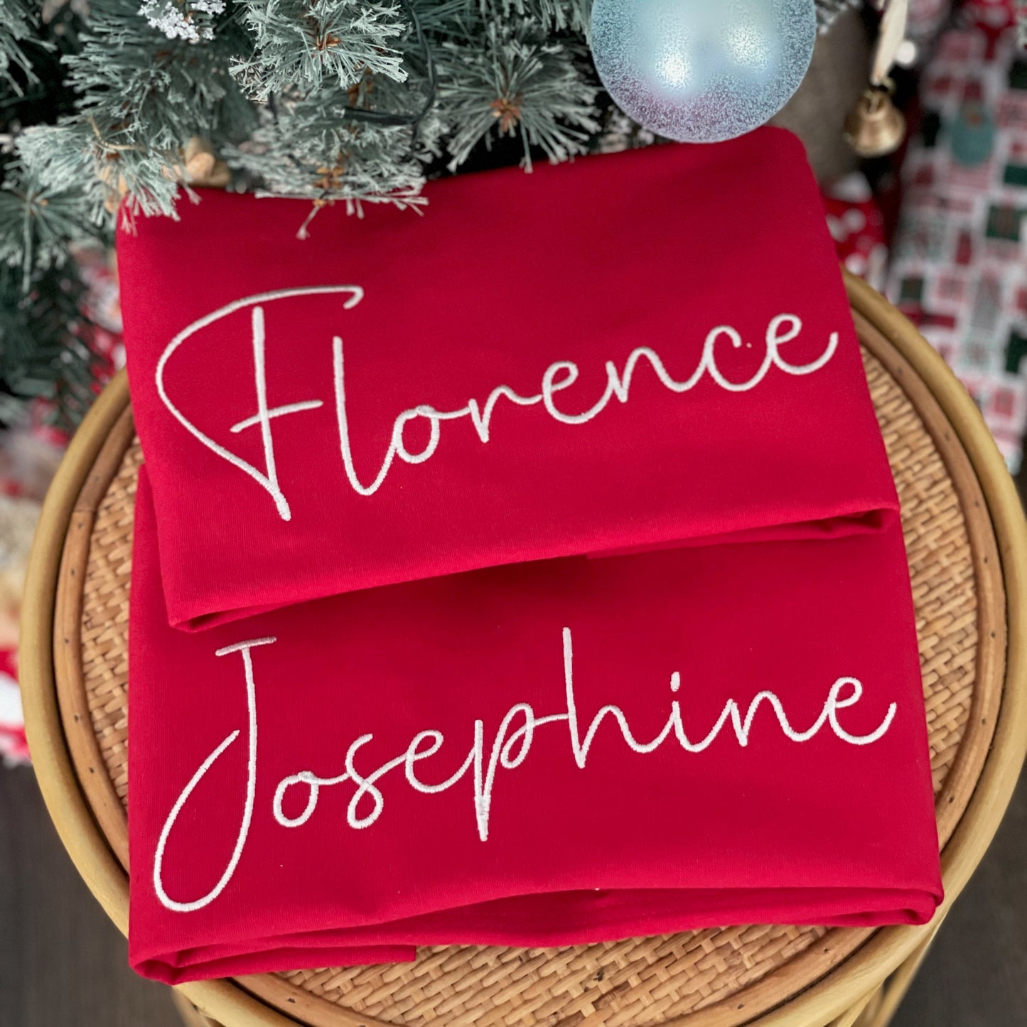 Red stockings with 'Florence' and 'Josephine' printed on them, placed under a Christmas tree.