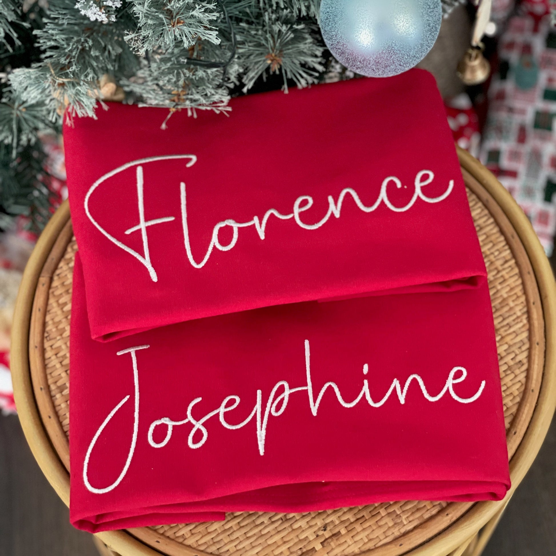 Red stockings with 'Florence' and 'Josephine' printed on them, placed under a Christmas tree.