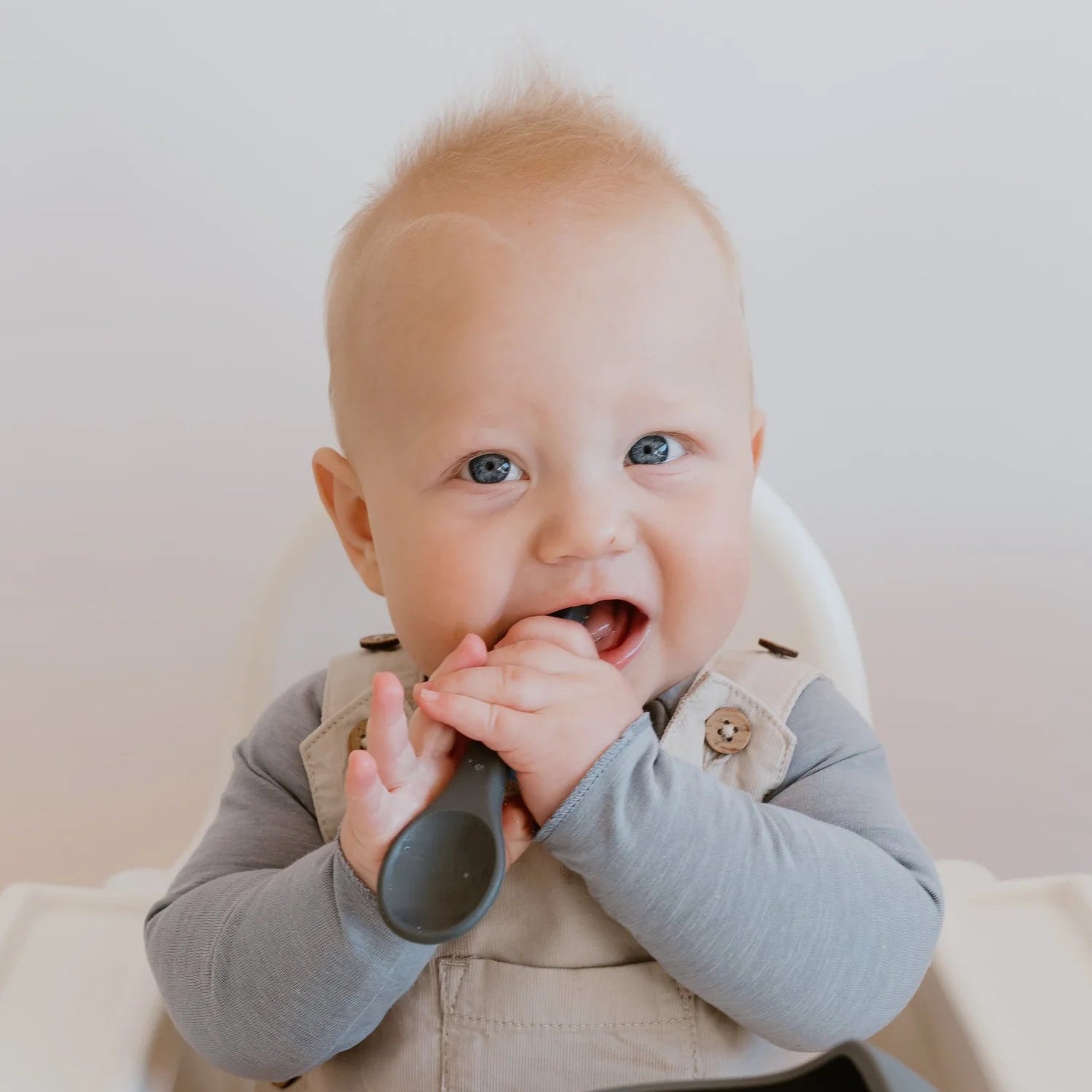 Baby sitting in a high chair with a bowl and spoon, smiling.