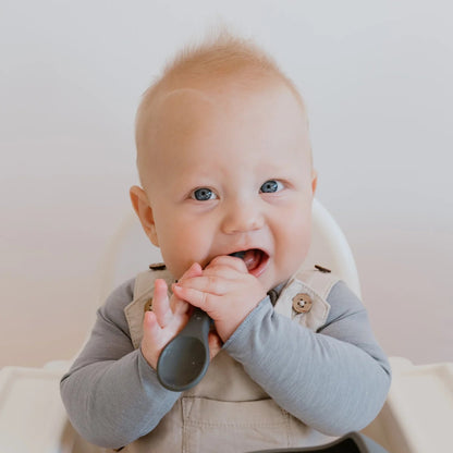 Baby sitting in a high chair with a bowl and spoon, smiling.