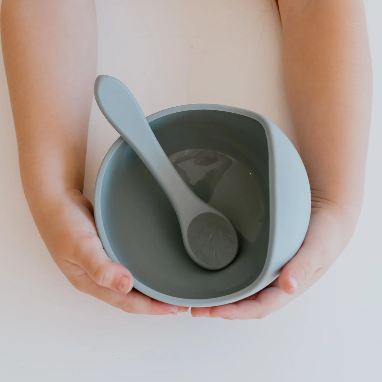 Person holding a gray ceramic bowl with a matching spoon on a light background