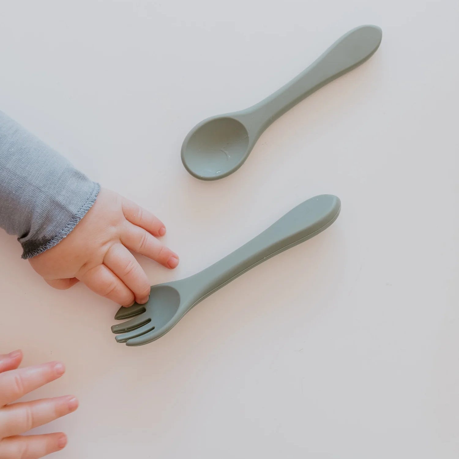 Two green spoons on a light surface with a child's hand reaching towards them.