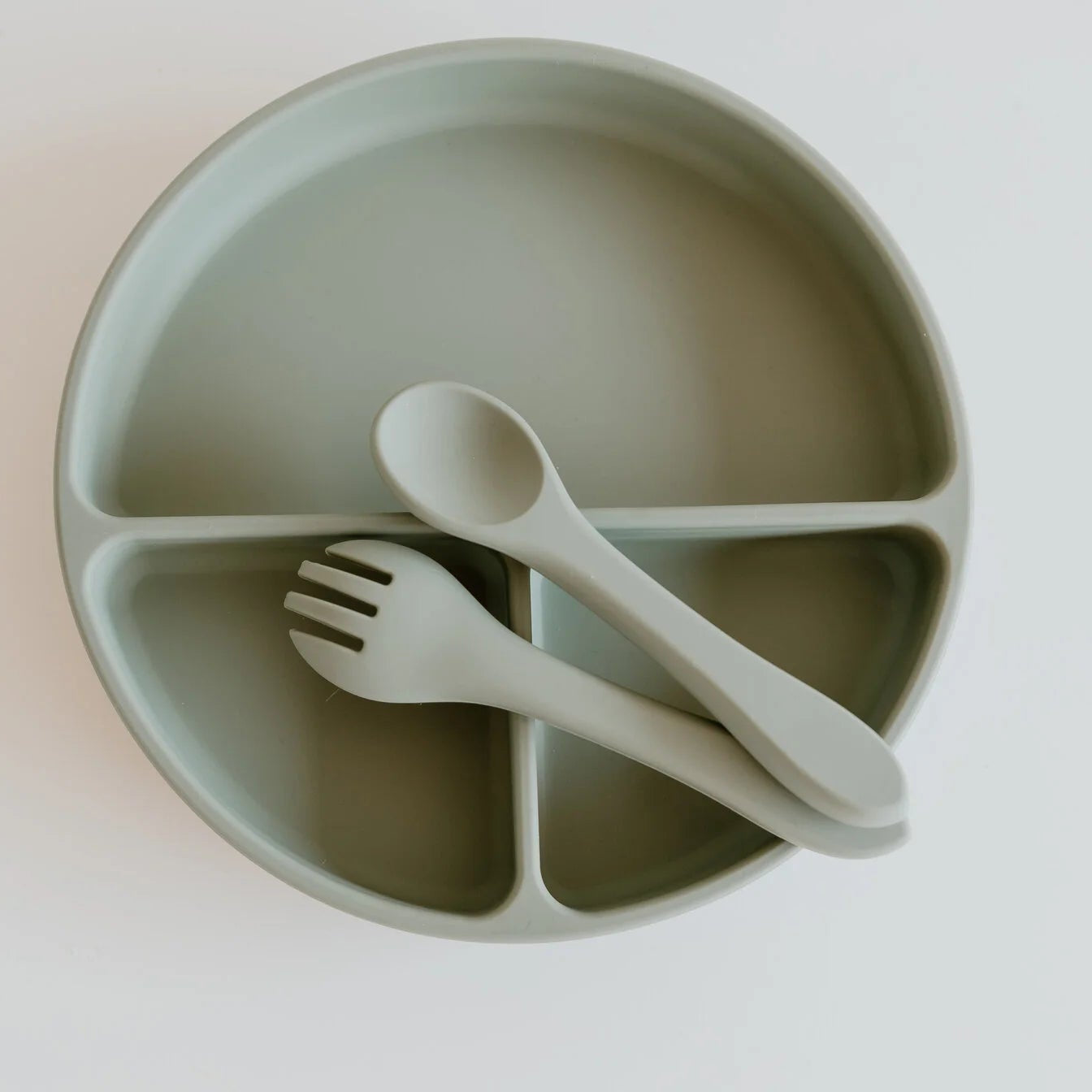 Children's green divided plate with fork and spoon on a white background