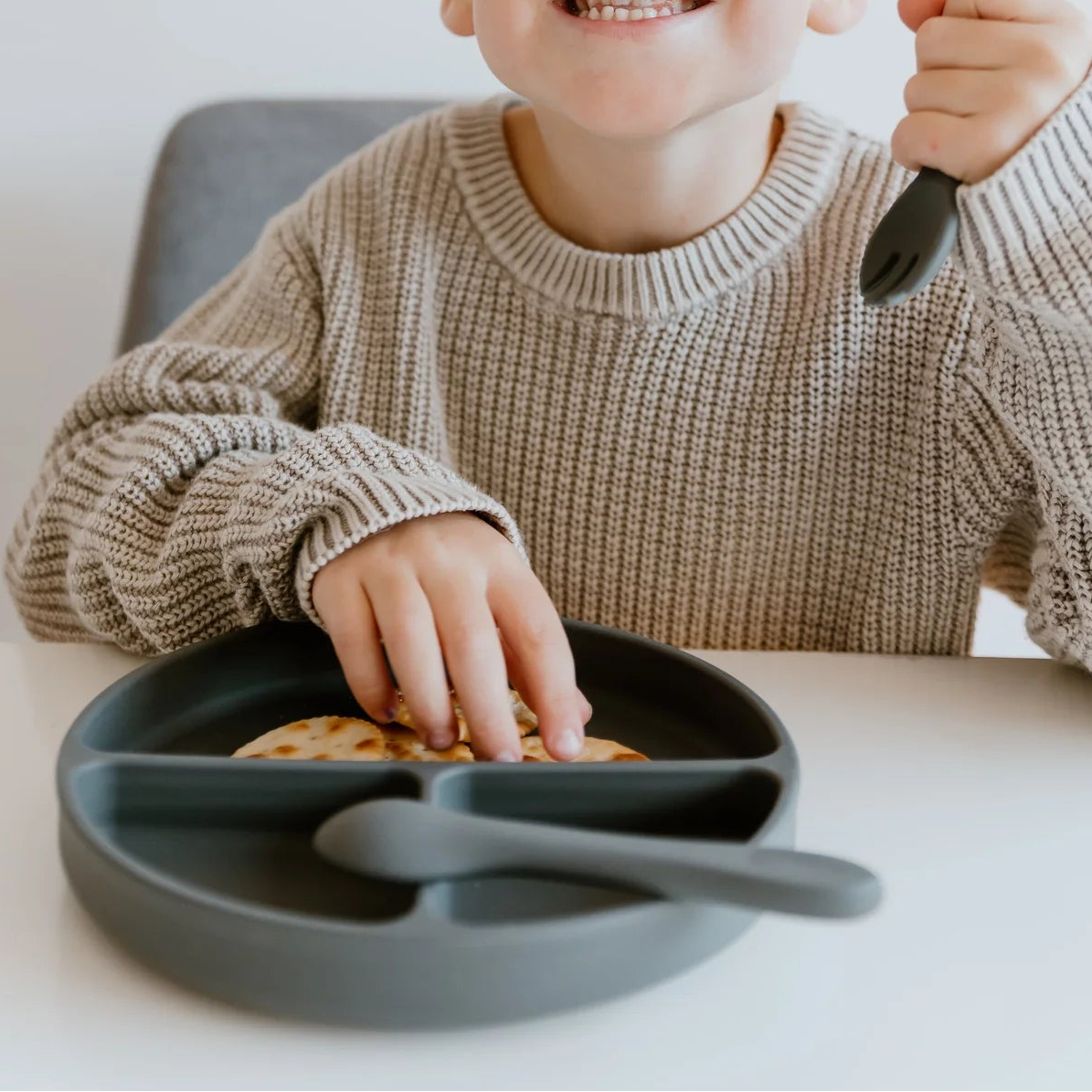 Child holding a spoon with a plate of cookies on a white background