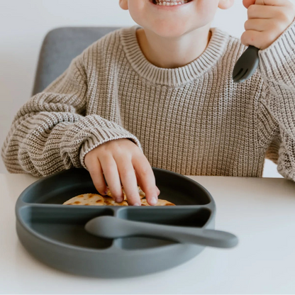 Child holding a spoon with a plate of cookies on a white background